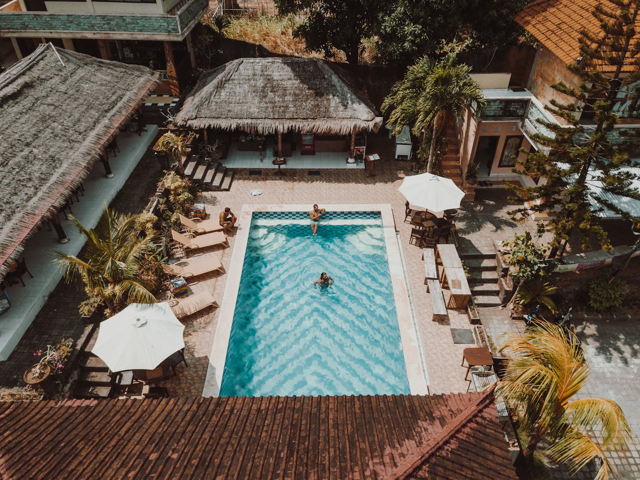 Offerings Aerial view of a luxury resort pool surrounded by villas and palm trees.